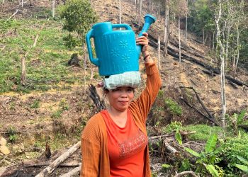 Nur Cahaya menjunjung gembor berisi air yang diambil dari sungai di lekuk bukit. Di belakangnya, lereng yang terbakar saat kemarau. (Foto: Dokumentasi Dorel Efendi)
